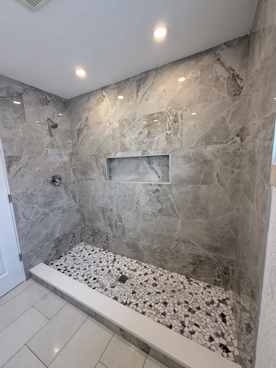 Gray tiled shower with recessed shelf and mosaic shower floor