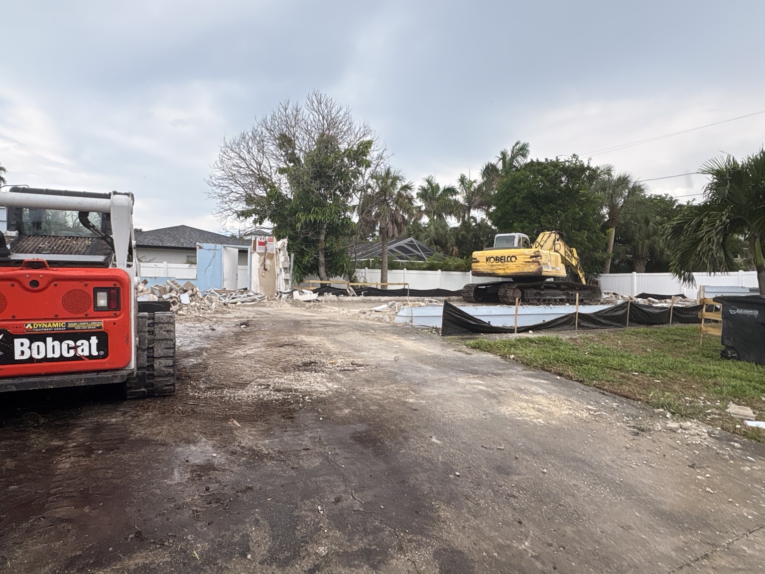 Building demolition in progress with excavator, skid steer and protected trees