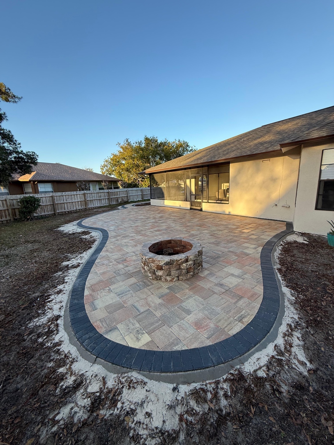 Curved backyard paver patio with a central stone fire pit